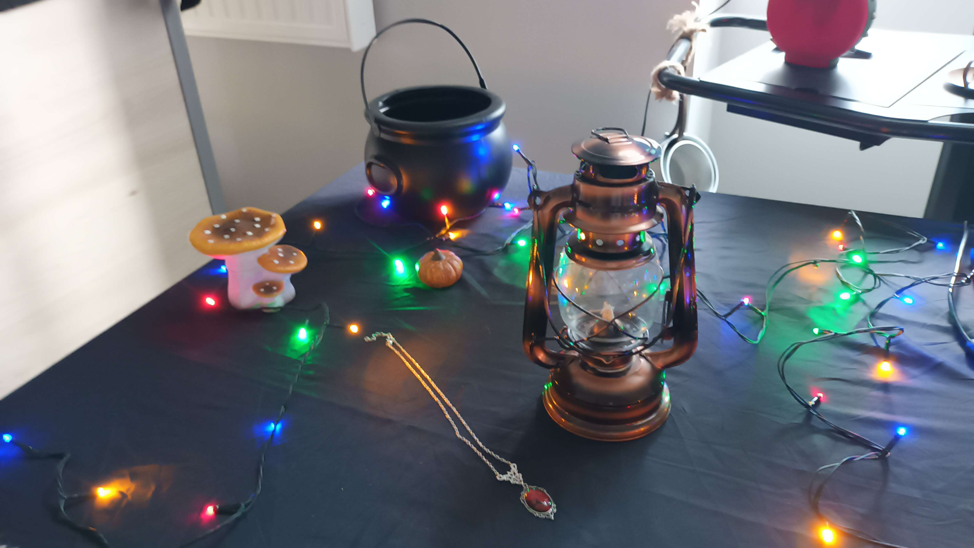 Photographie de diverses babioles (une lanterne, un pendentif, un chaudron) qui décorent une table, entourés d'une guirlande multicolore lumineuse