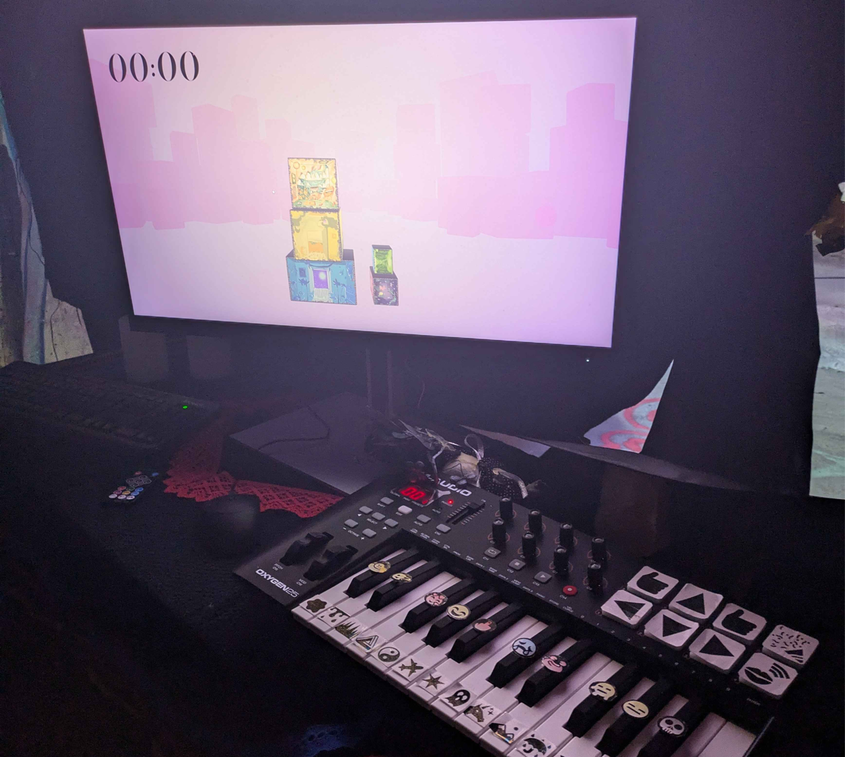 Photographie d'un clavier de piano avec des émojis collée sur les touches, devant un écran qui affiche une pile de cubes numériques